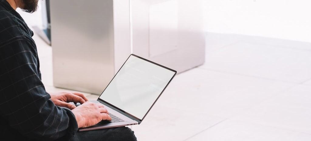 Side view of crop bearded male in casual outfit browsing laptop with empty screen while sitting on sofa in contemporary IOP program